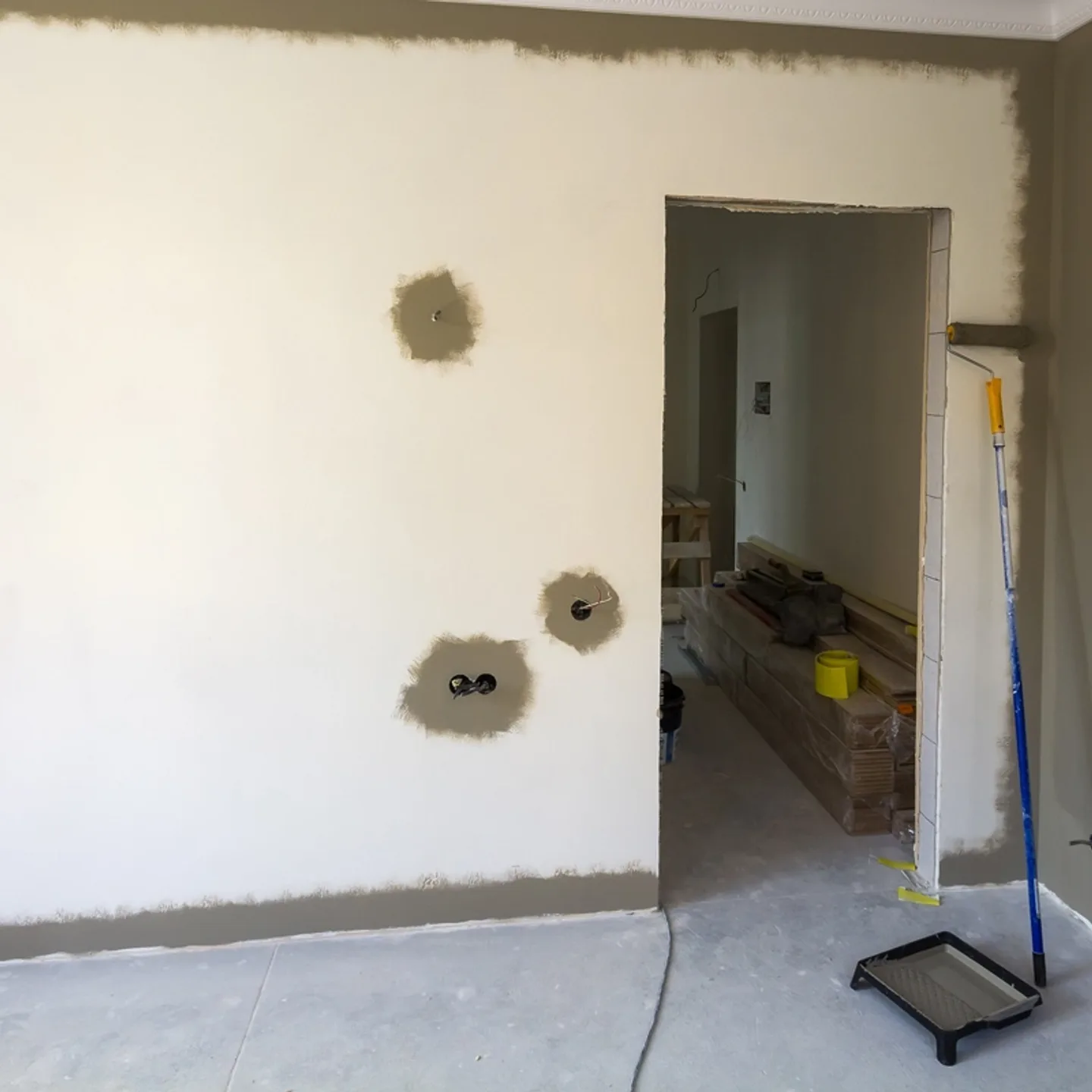 Frisch gespachtelte Wand mit Malerrolle und vorbereiteten Steckdosenauslässen